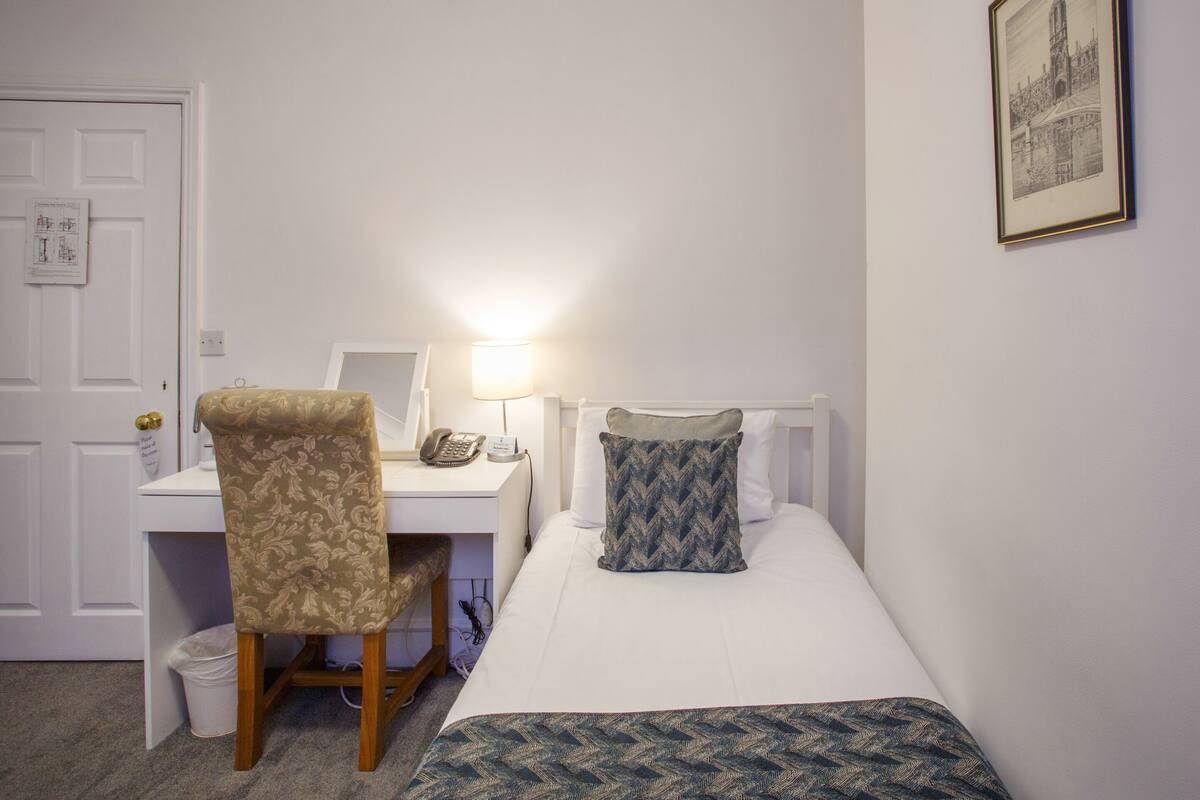 A hotel room with a bed, a desk with a chair, a lamp, and a framed picture on the wall.