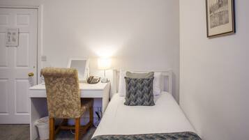 A hotel room with a bed, a desk with a chair, a lamp, and a framed picture on the wall.