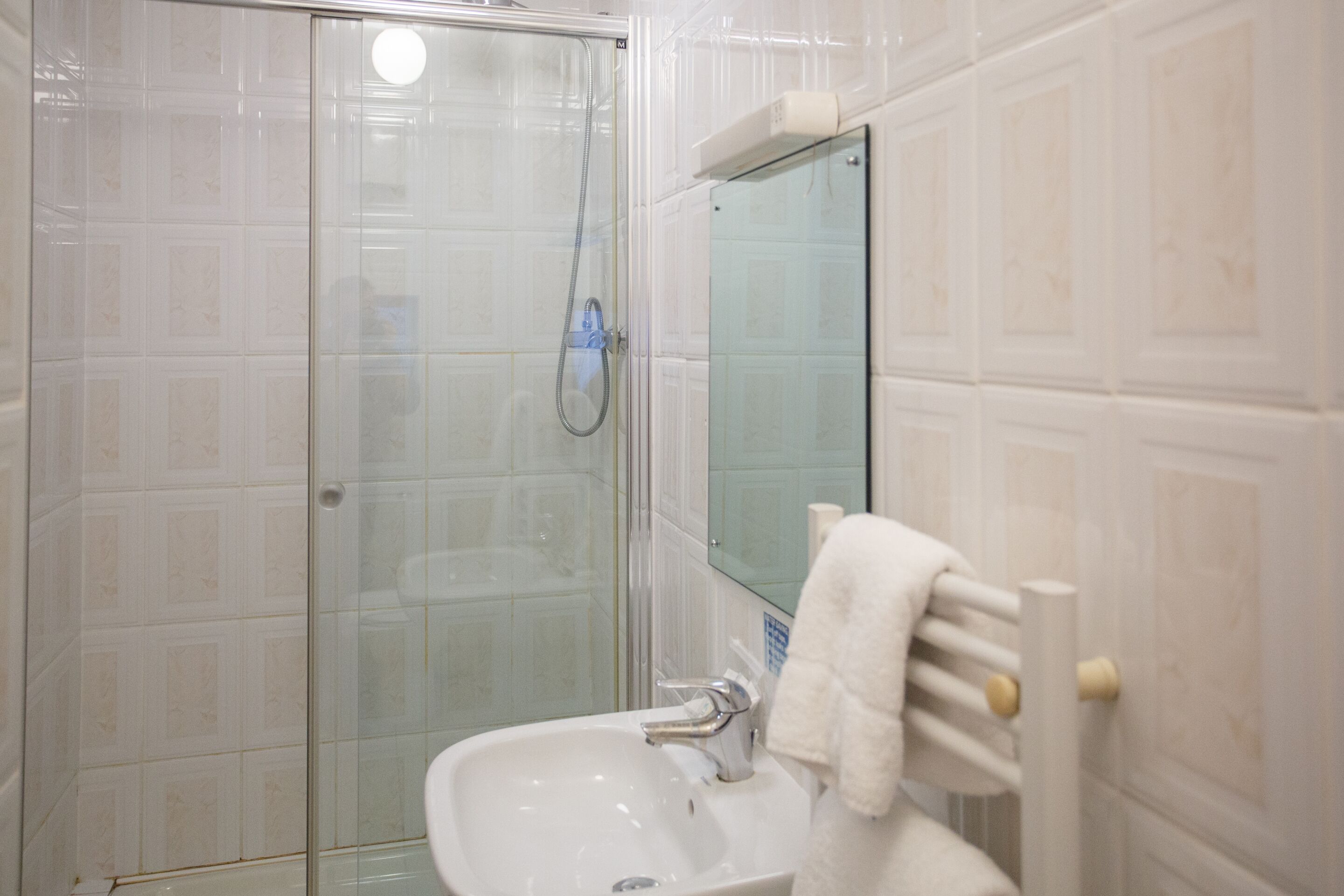 Un baño con cabina de ducha de vidrio, un lavabo y un perchero para toallas.