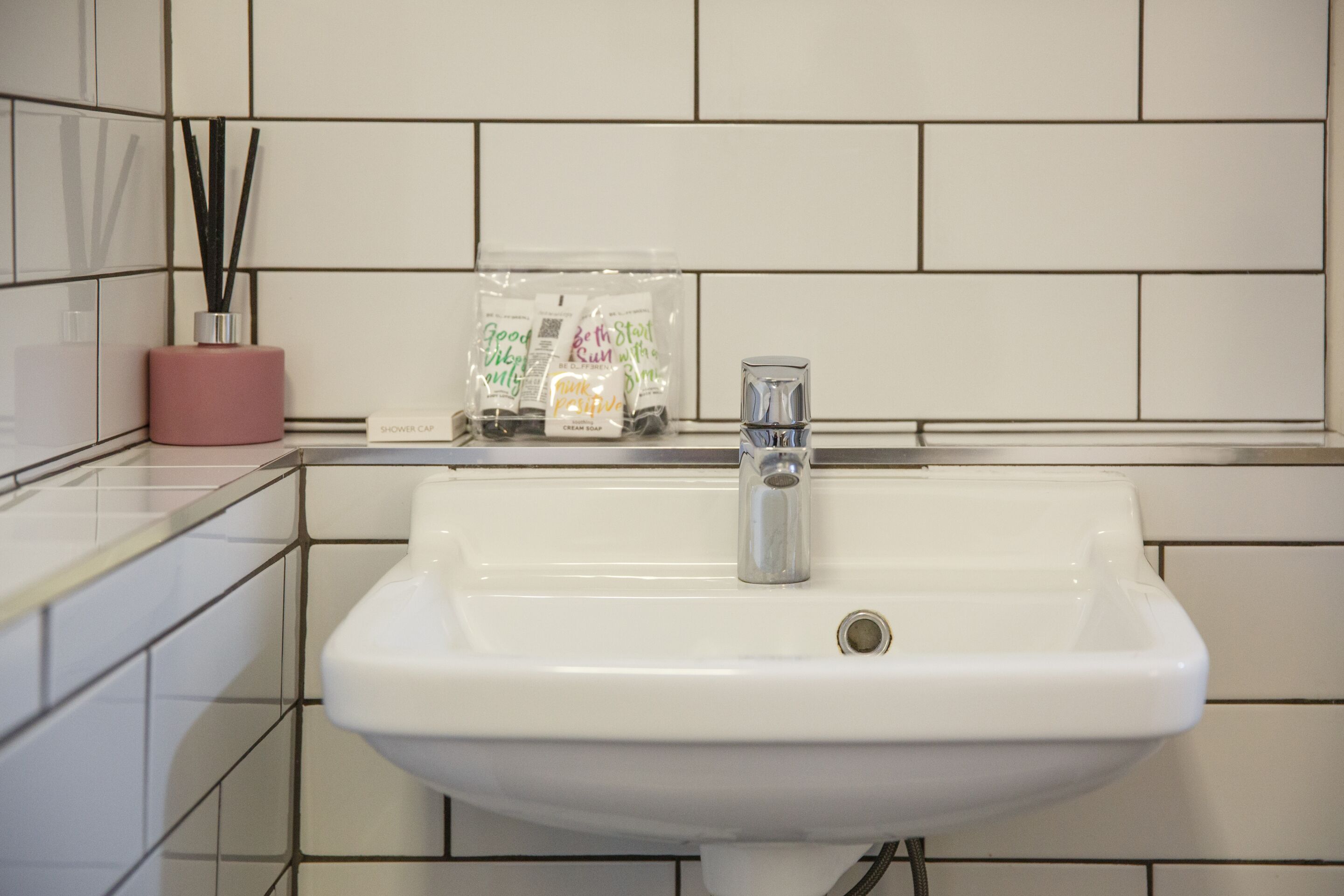 A white bathroom sink with a modern faucet, a pink soap dispenser, and a set of scented candles on the counter.