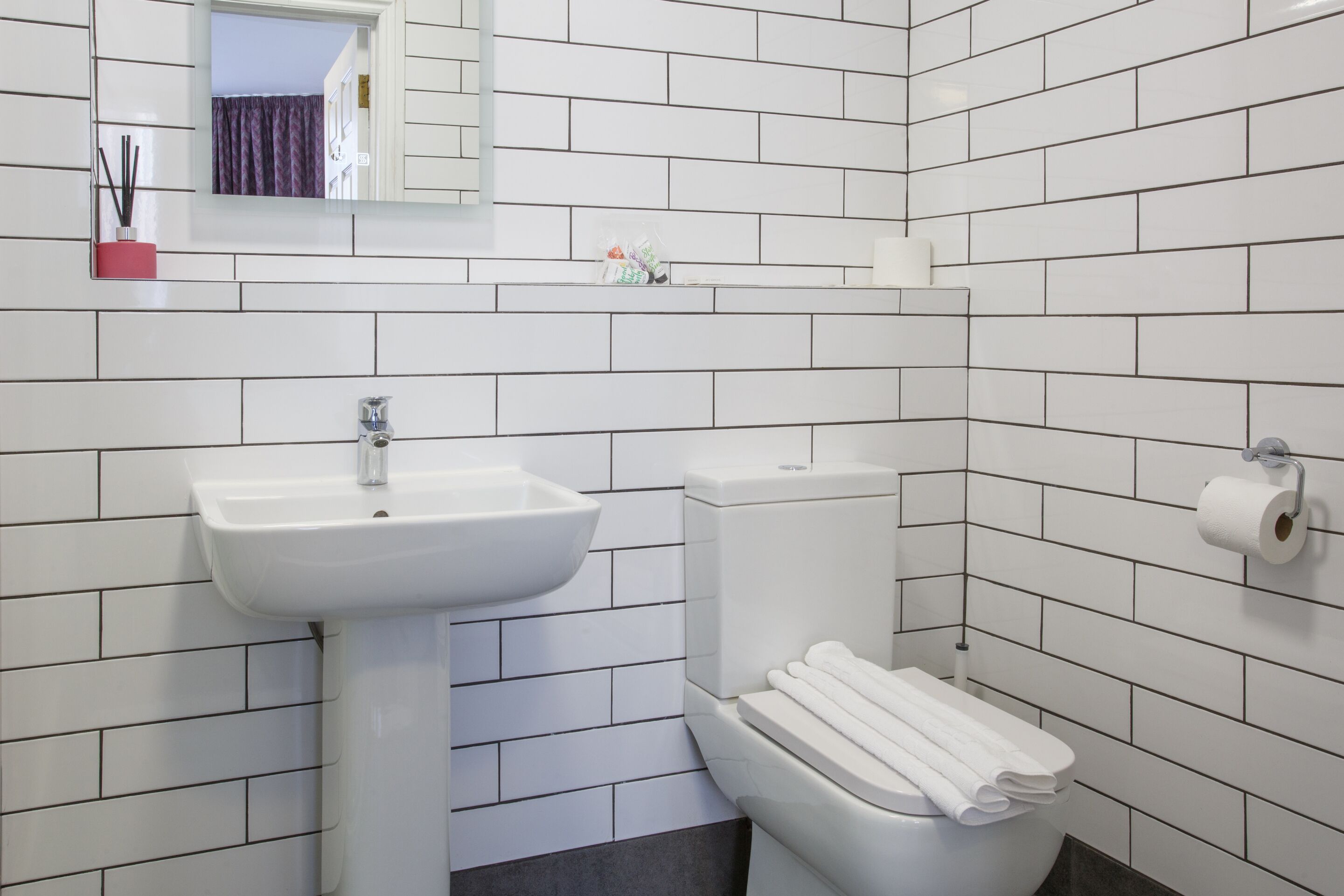 A bathroom with white tiled walls, a white sink, and a toilet.