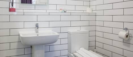 A bathroom with white tiled walls, a white sink, and a toilet.