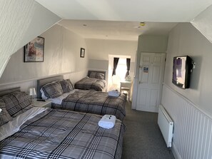 A bedroom with two beds, a bedside table with a lamp, a framed picture on the wall, and a radiator. - The Cara Guesthouse (Whitley Bay)
