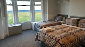 A bedroom with two beds, a view of a grassy field, and a bench by the window. - The Cara Guesthouse (Whitley Bay)