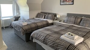 A hotel room with two beds, a desk, and a window. - The Cara Guesthouse (Whitley Bay)