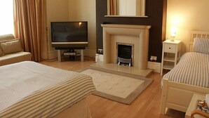 A hotel room with a fireplace, a television, a bed, a sofa, and a bedside table. - The Cara Guesthouse (Whitley Bay)