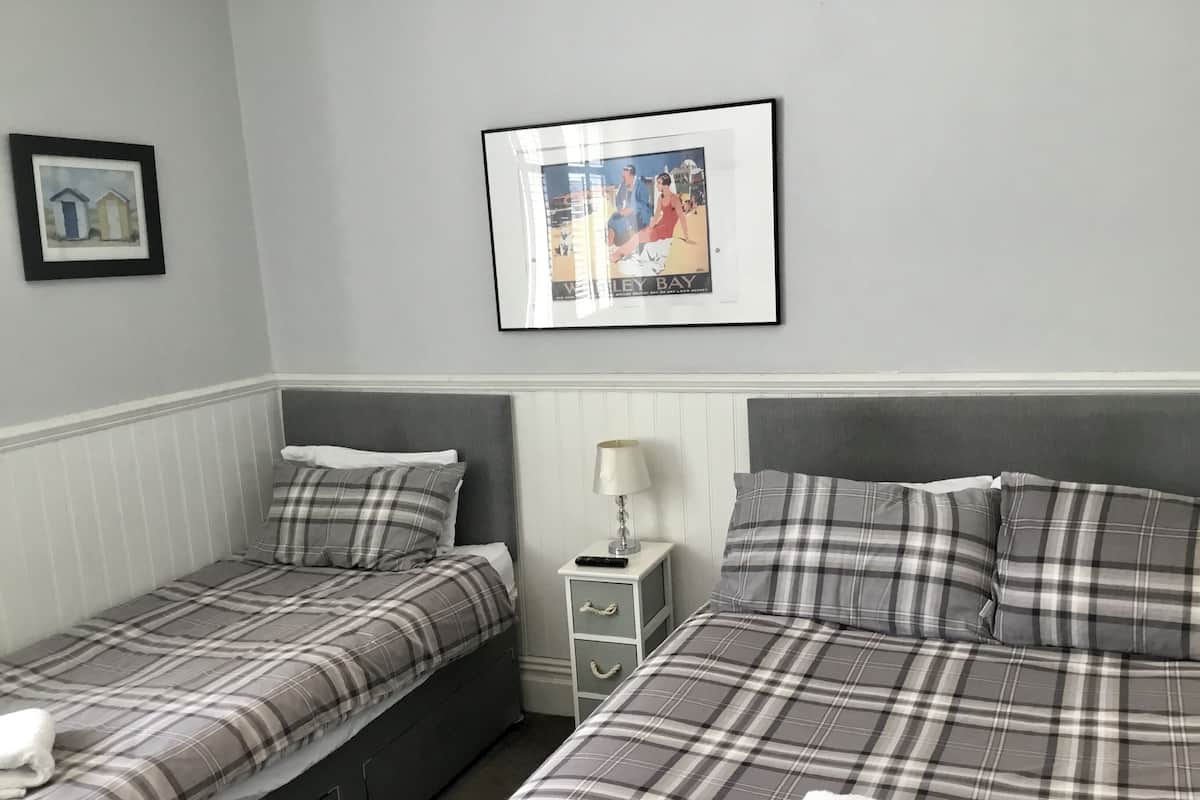 Una habitación con dos camas, cada una con colcha y almohadas a cuadros grises y blancos. En la pared, sobre las camas, hay un cuadro con una escena de playa.
