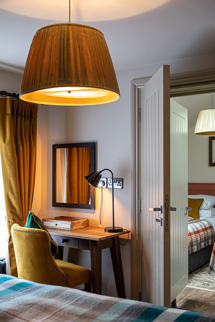 Une chambre d’hôtel comprenant un lit, un bureau avec une lampe, une chaise, un miroir et une porte donnant sur une autre pièce.