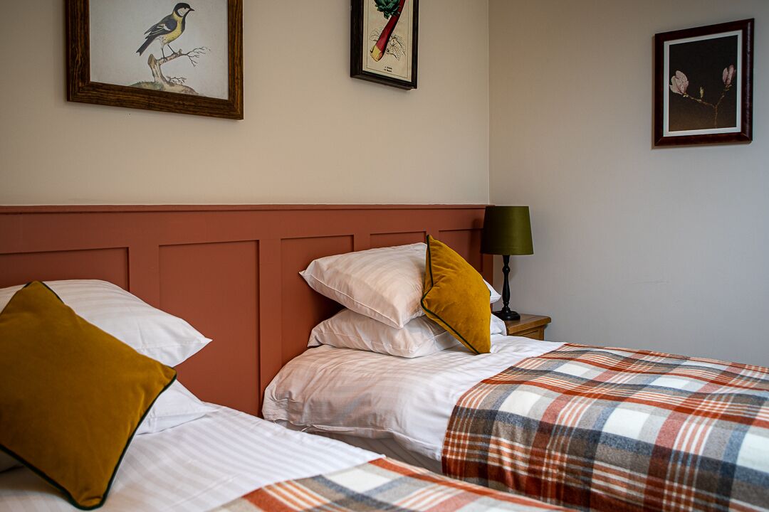 Ein Hotelzimmer mit einem Bett, Kissen, einem Nachttisch, einer Lampe und gerahmten Bildern an der Wand.