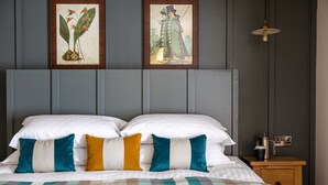 A neatly made bed with white and teal pillows, a plaid blanket, and two framed botanical prints on the wall above. - The Filly Inn (Brockenhurst)