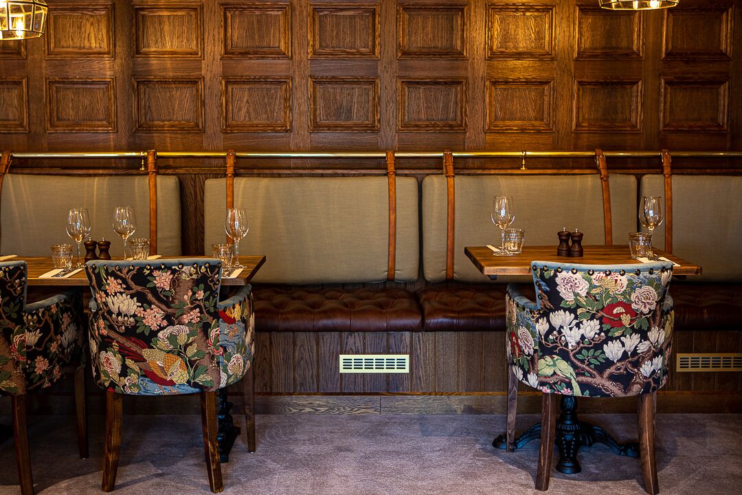 Interior de restaurante com paredes de painel de madeira, assentos estofados e cadeiras com padrão floral.