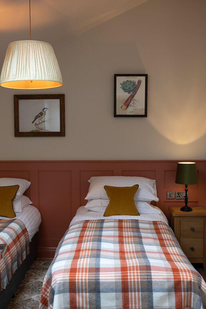 A hotel room with two beds, a large window, a wall-mounted lamp, and framed artwork.