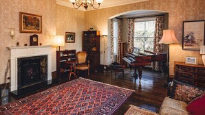 A room with a fireplace, a piano, a large rug, and a chandelier. - The Forest Country House B&B (Newtown)