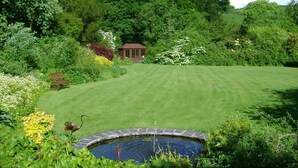 A well-maintained garden with a lawn, a small pond, and a wooden bench. - The Forest Country House B&B (Newtown)