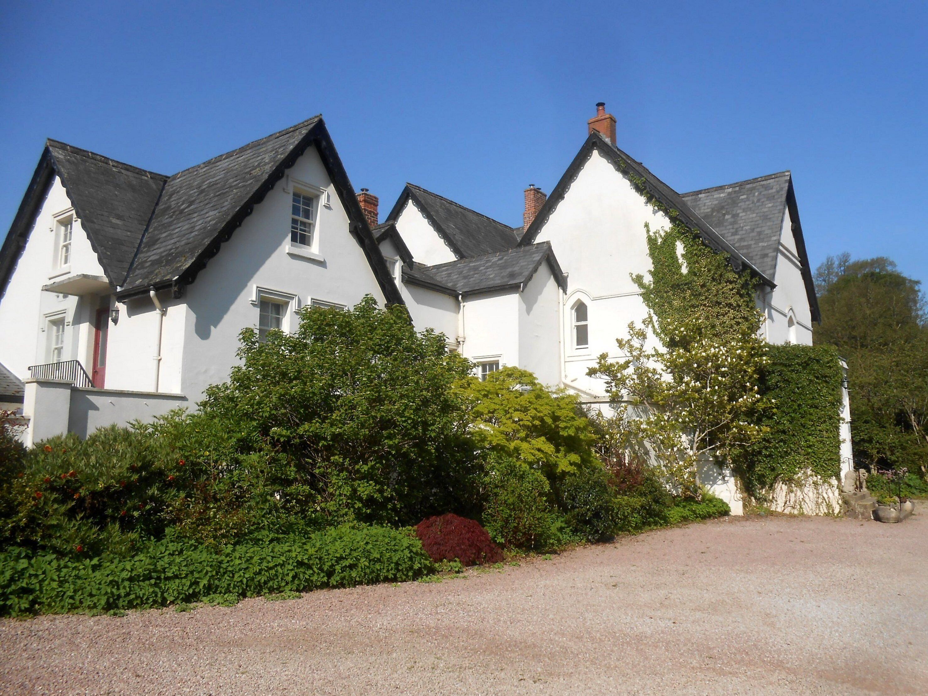 Une grande maison blanche avec de nombreuses cheminées et une allée gravillonnée.