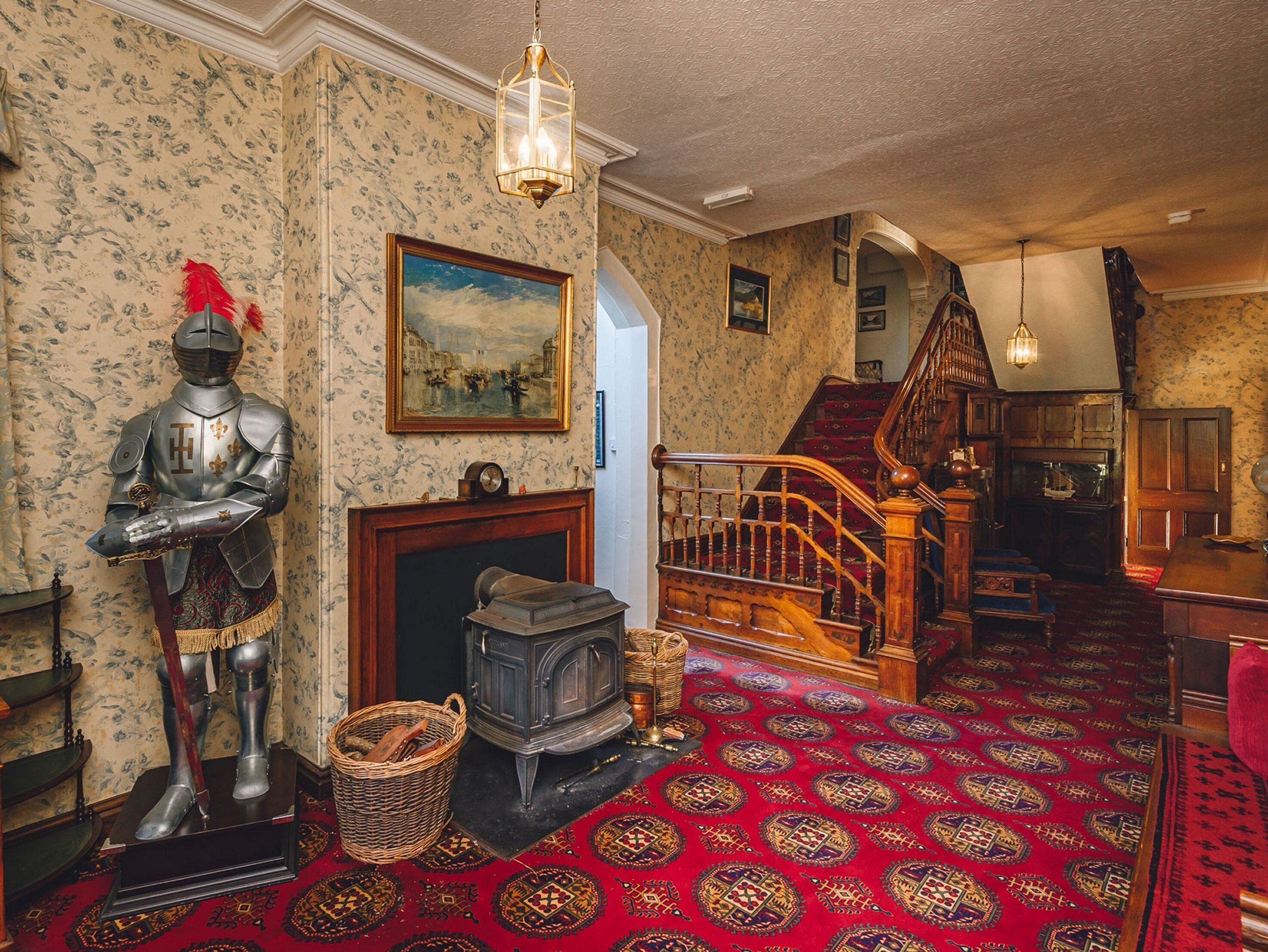 Una habitación con chimenea, una escalera de madera y una estatua de un caballero medieval.