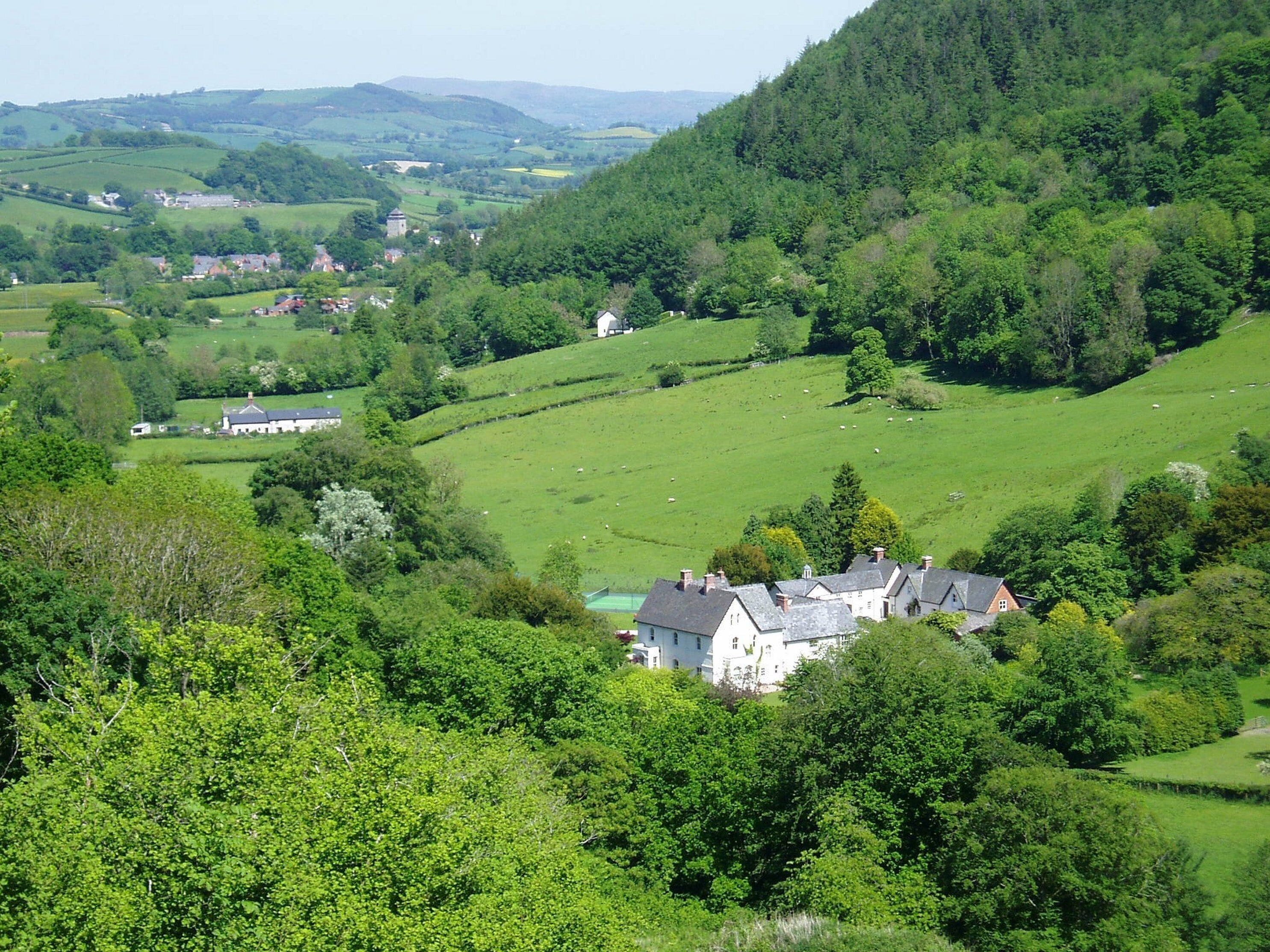 A rural landscape with rolling hills, a small cluster of houses, and a large white building with a green roof.