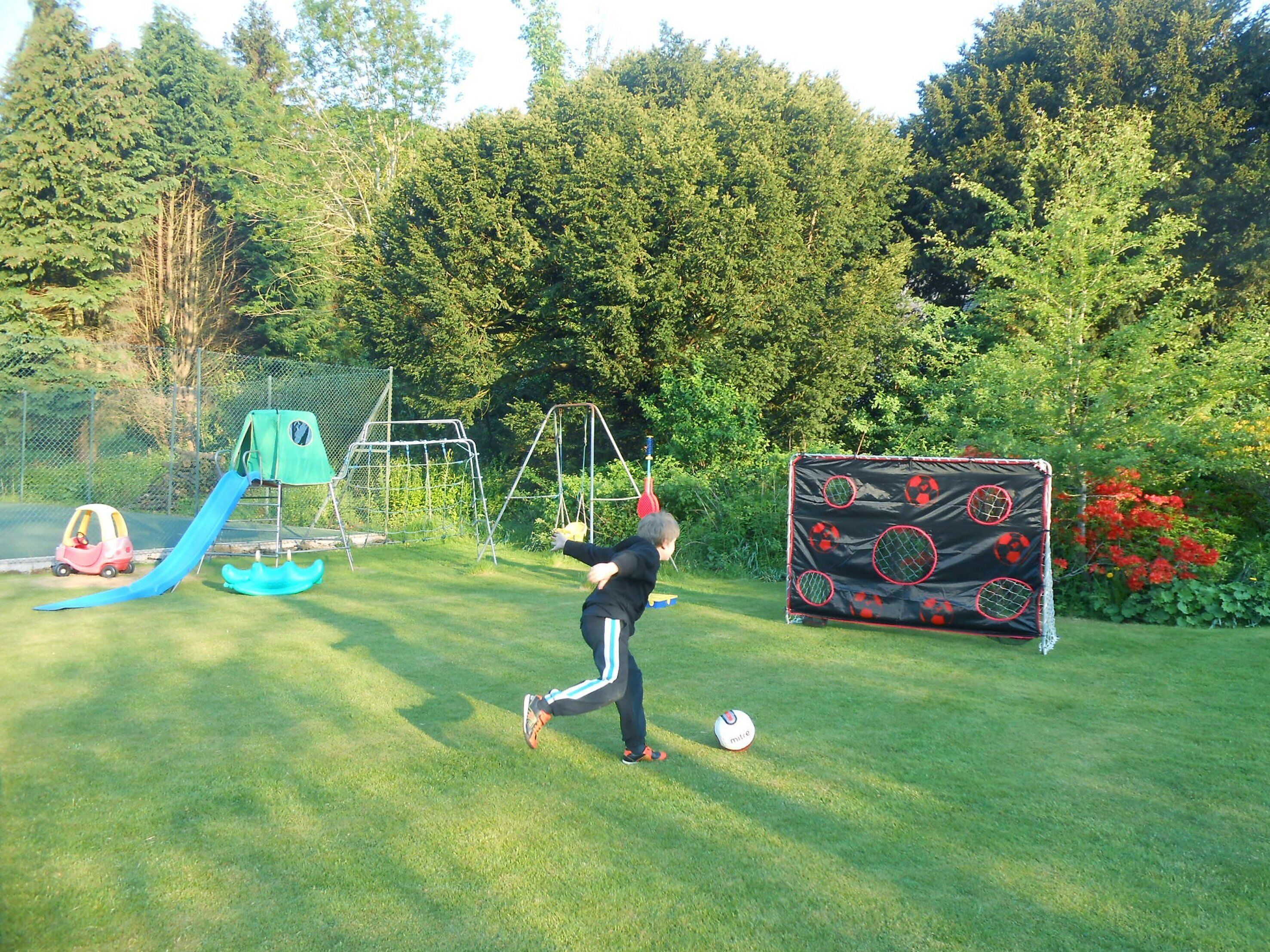 A grassy outdoor area with a soccer goal, a slide, and a swing set.