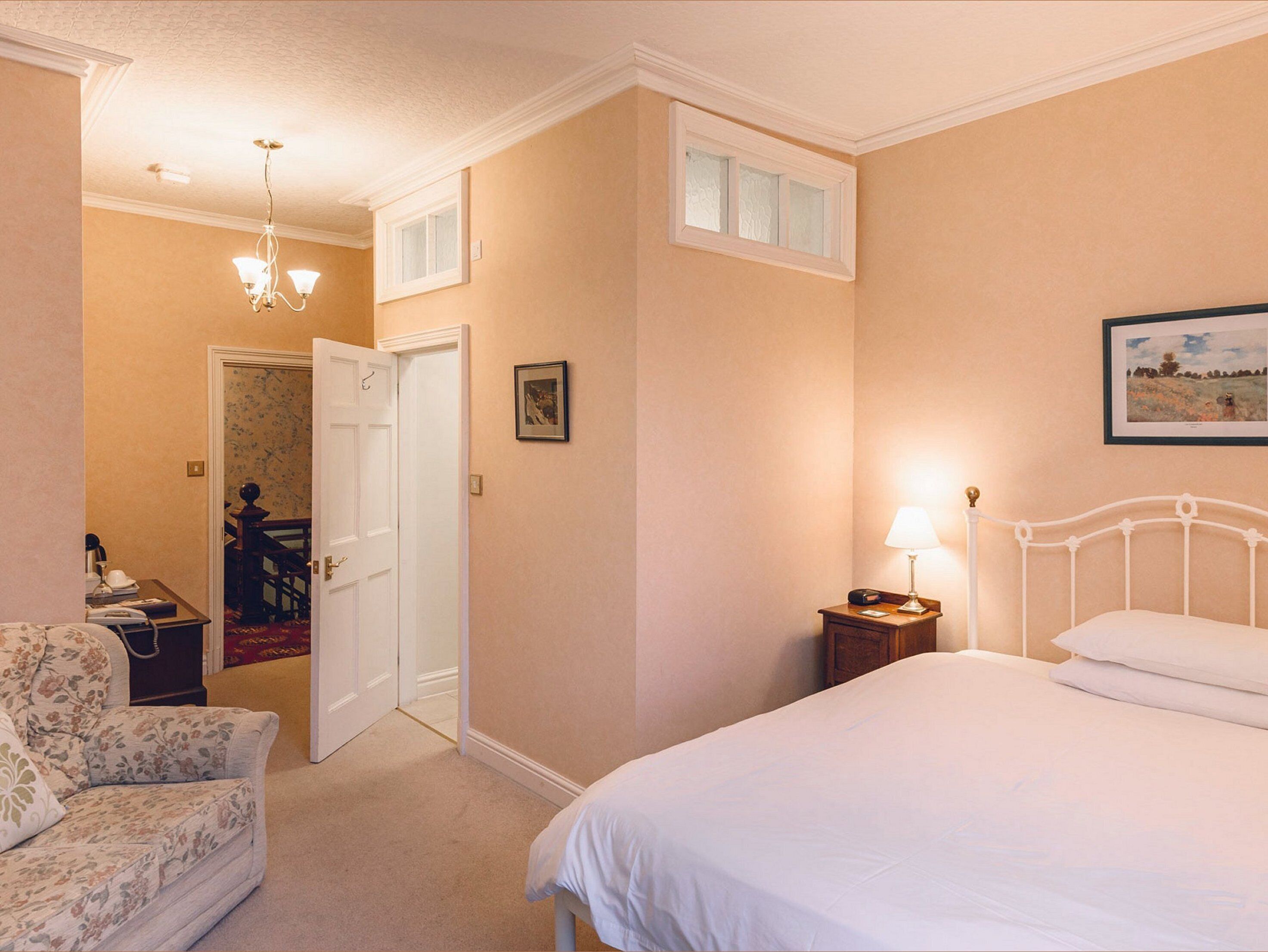 A bedroom with a bed, a nightstand, a lamp, a chair, a door, and a small table.