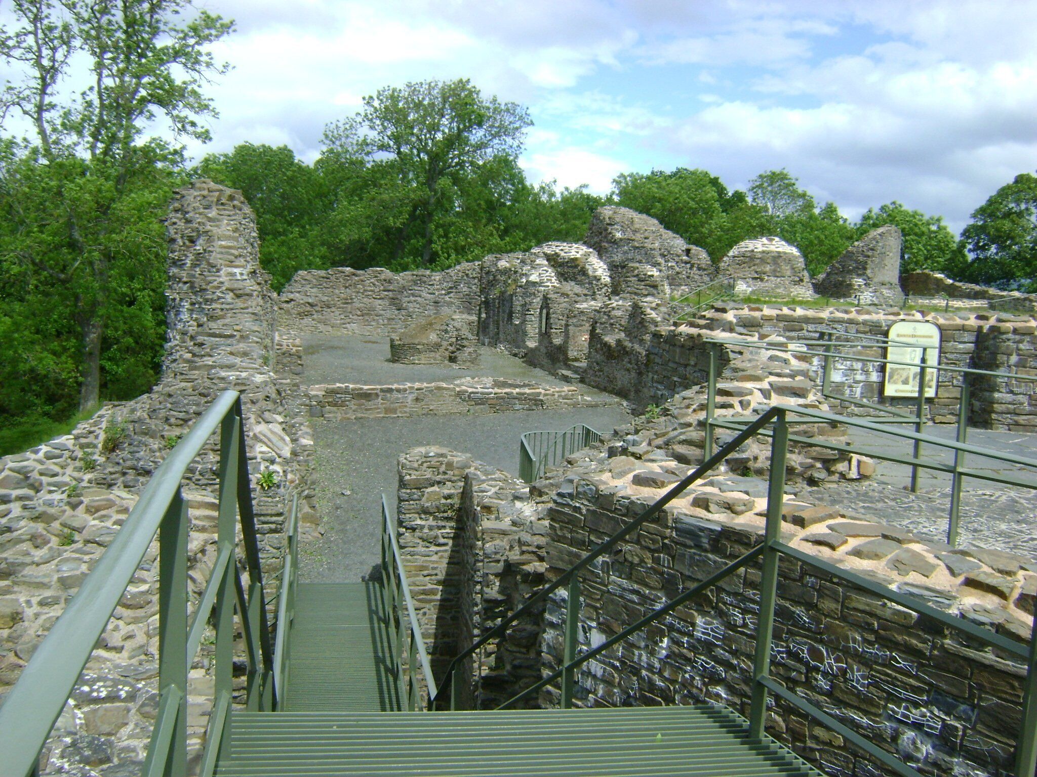 Un chemin de pierre mène à une ancienne construction en pierre, dotée d’un escalier et d’une rampe en métal.