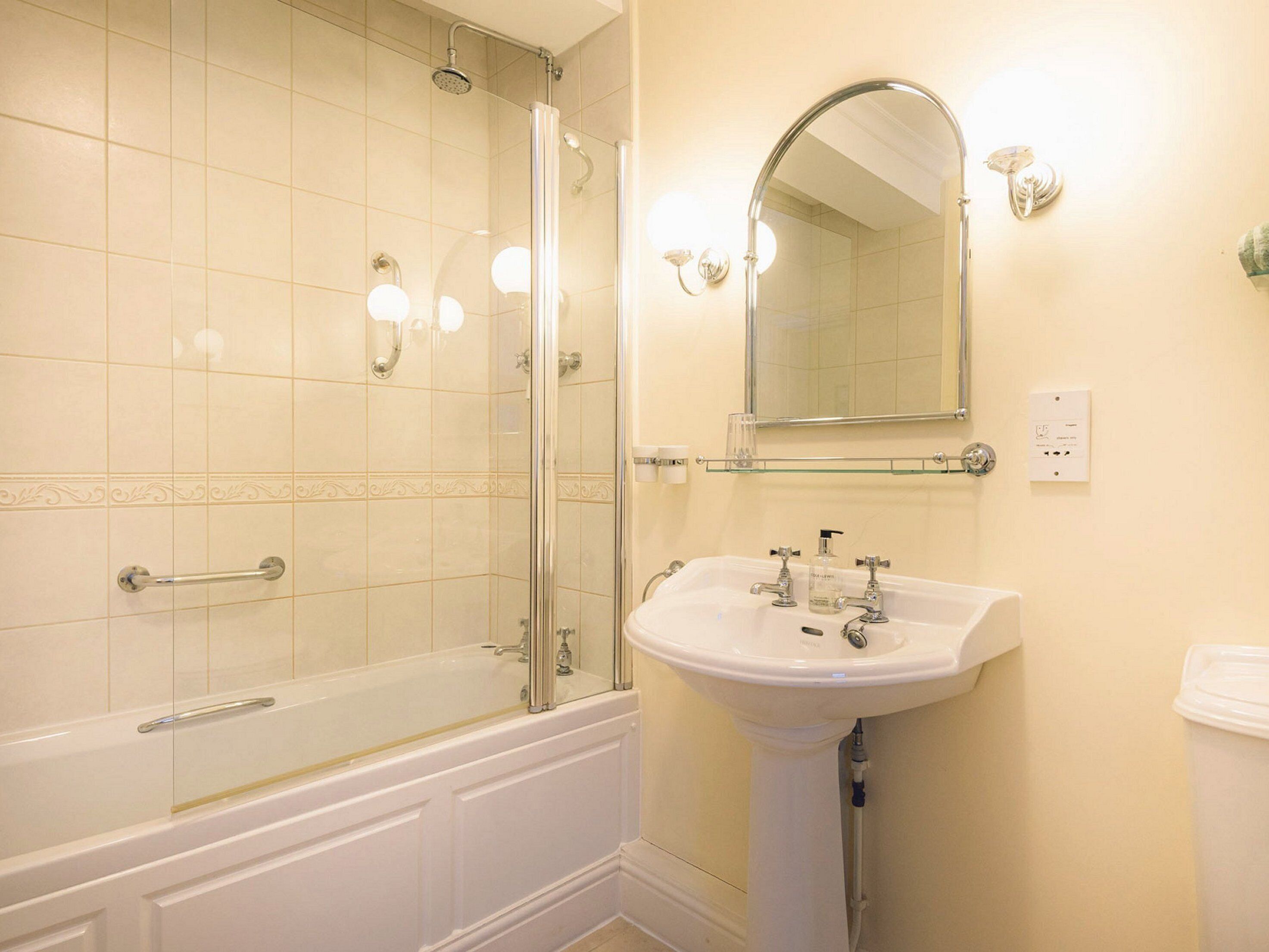 Un baño con ducha de vidrio, lavamanos pedestal y espejo sobre el lavamanos.