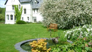 A large white building with a garden, a pond, and a wooden sign. - The Forest Country House B&B (Newtown)