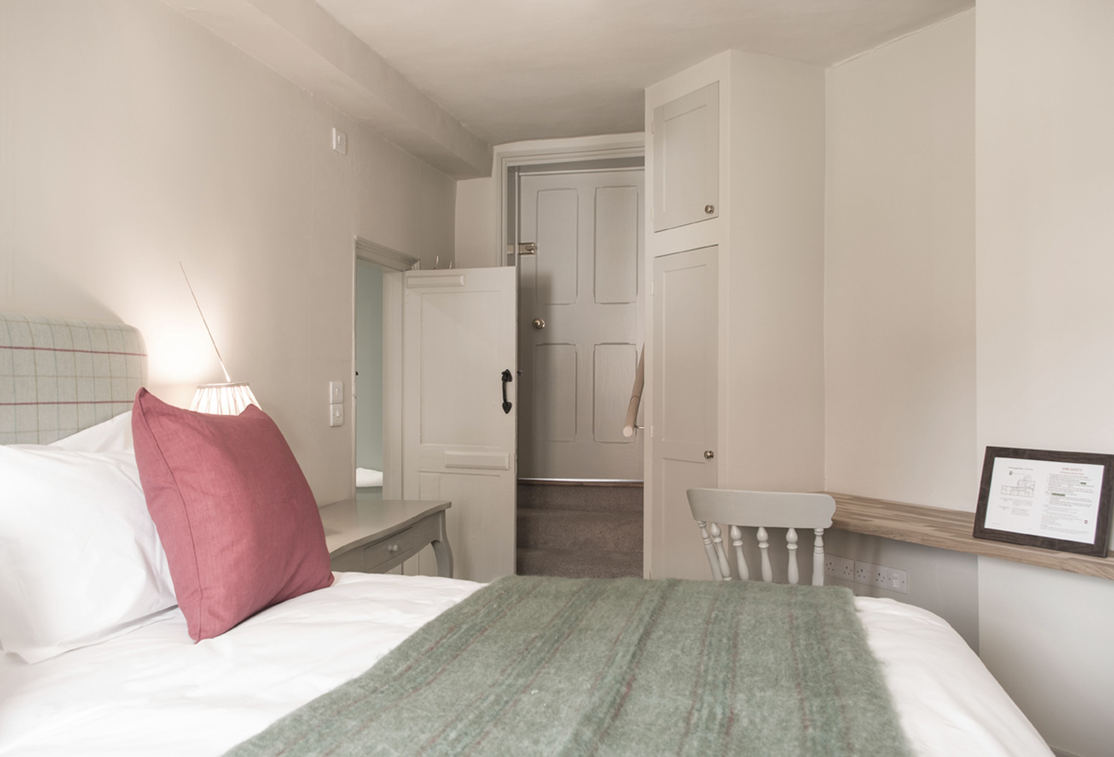 A bedroom with a bed, a nightstand, a chair, a door, and a wall-mounted shelf.