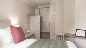 A bedroom with a bed, a nightstand, a chair, a door, and a wall-mounted shelf.