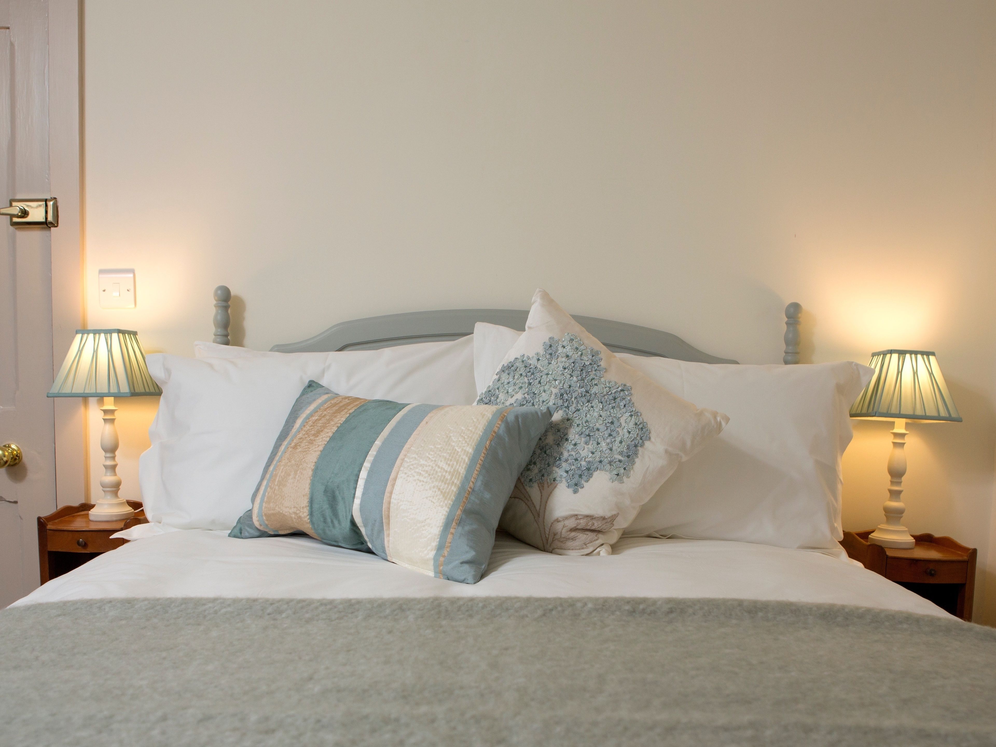A neatly made bed with white bedding and multiple pillows, two bedside lamps, and a wooden nightstand.