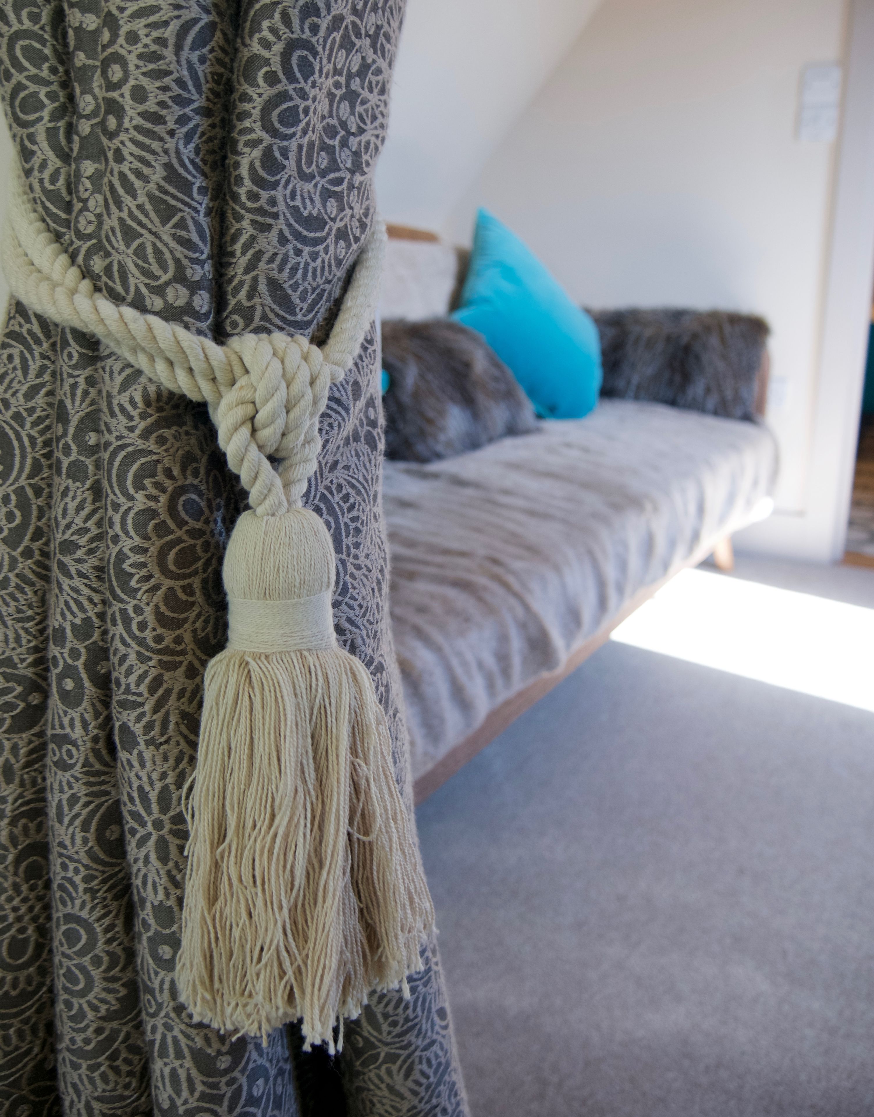 Ein Zimmer mit einem Bett, einem Vorhang mit Quaste und einem Kissen.