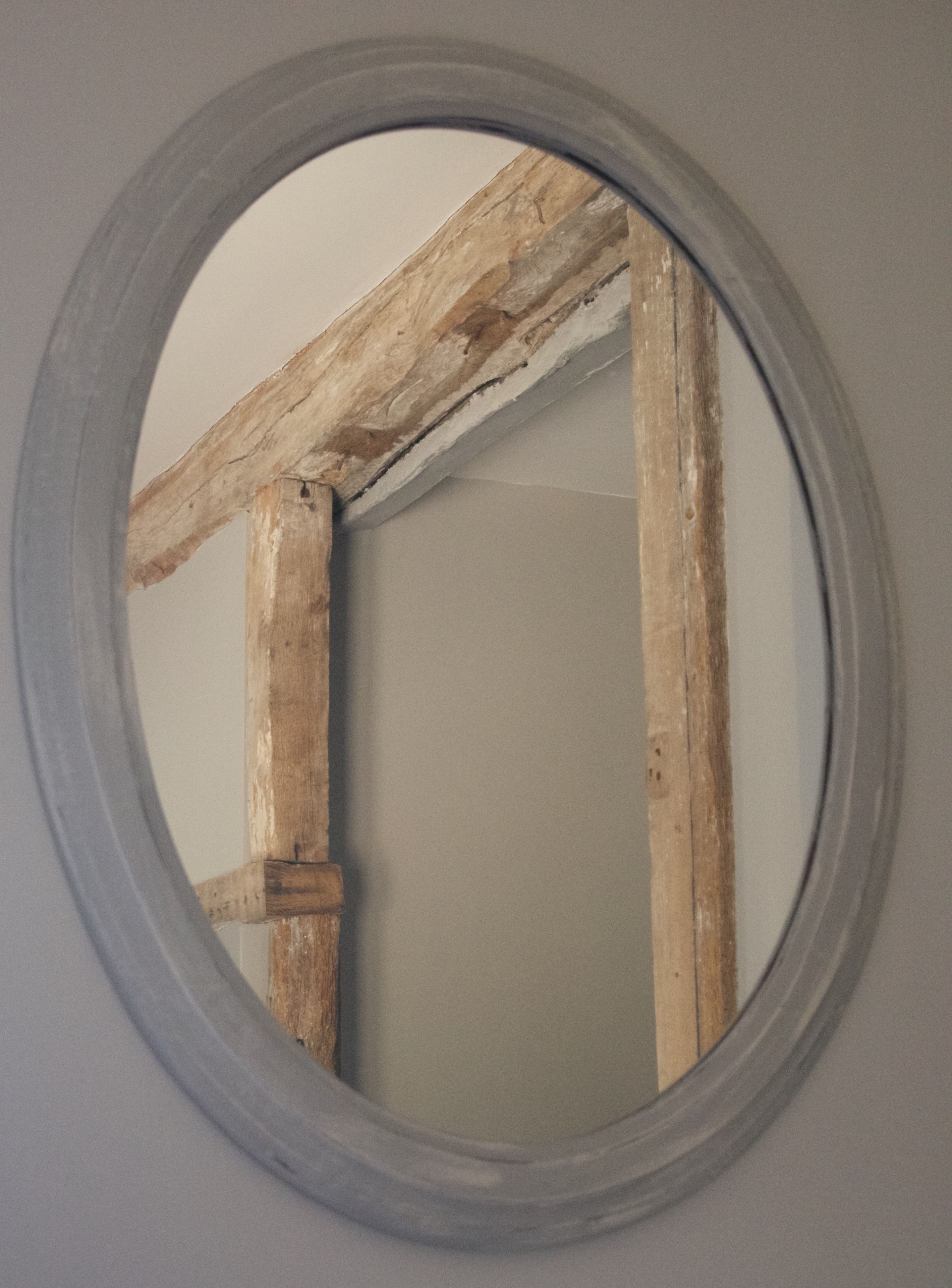 Espejo redondo con marco de madera que refleja parte de una habitación.