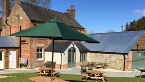 A patio area with wooden picnic tables and a green umbrella. - The Greyhound Inn (Wantage)
