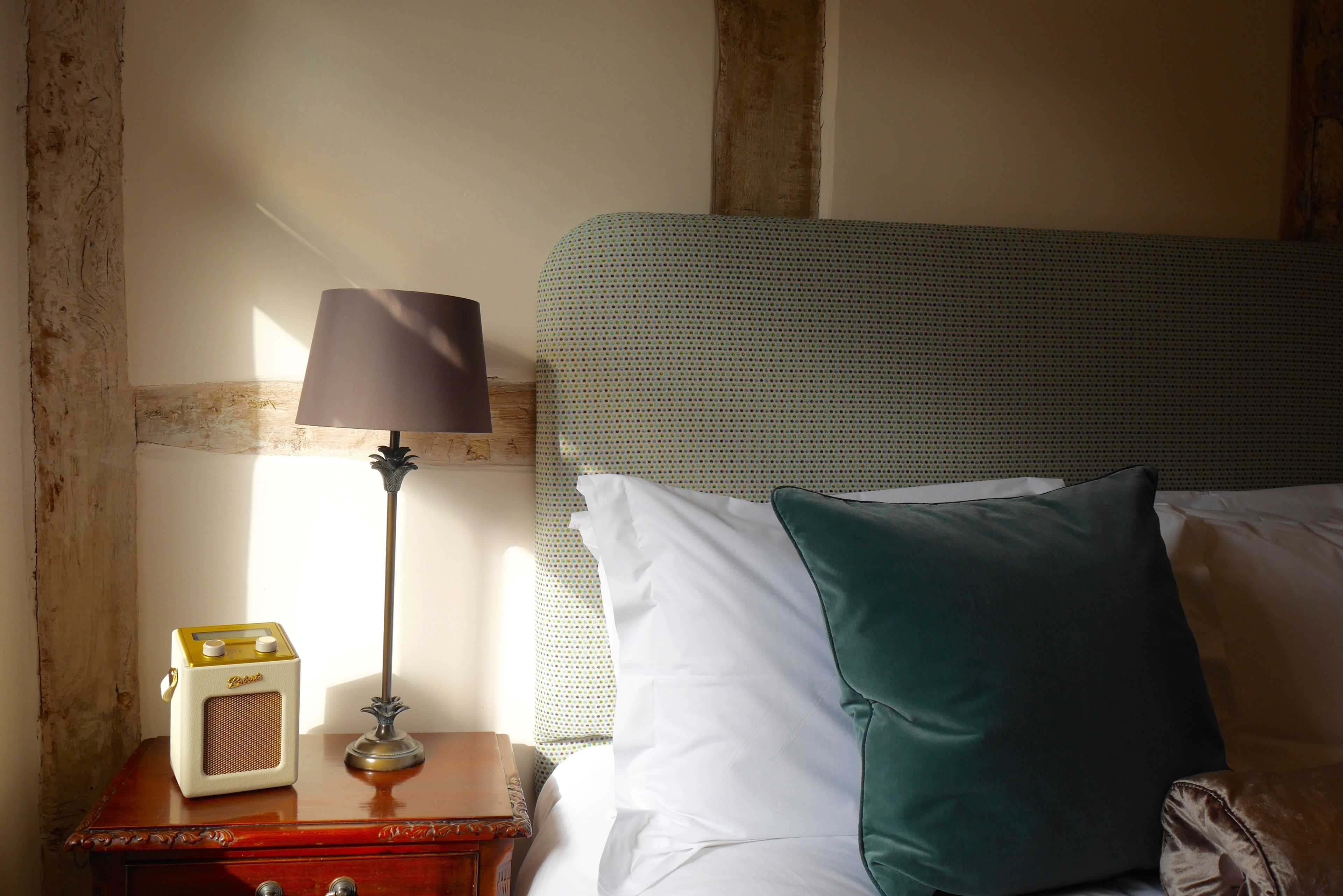 A neatly made bed with a green headboard, a bedside lamp, and a vintage radio on a wooden nightstand.