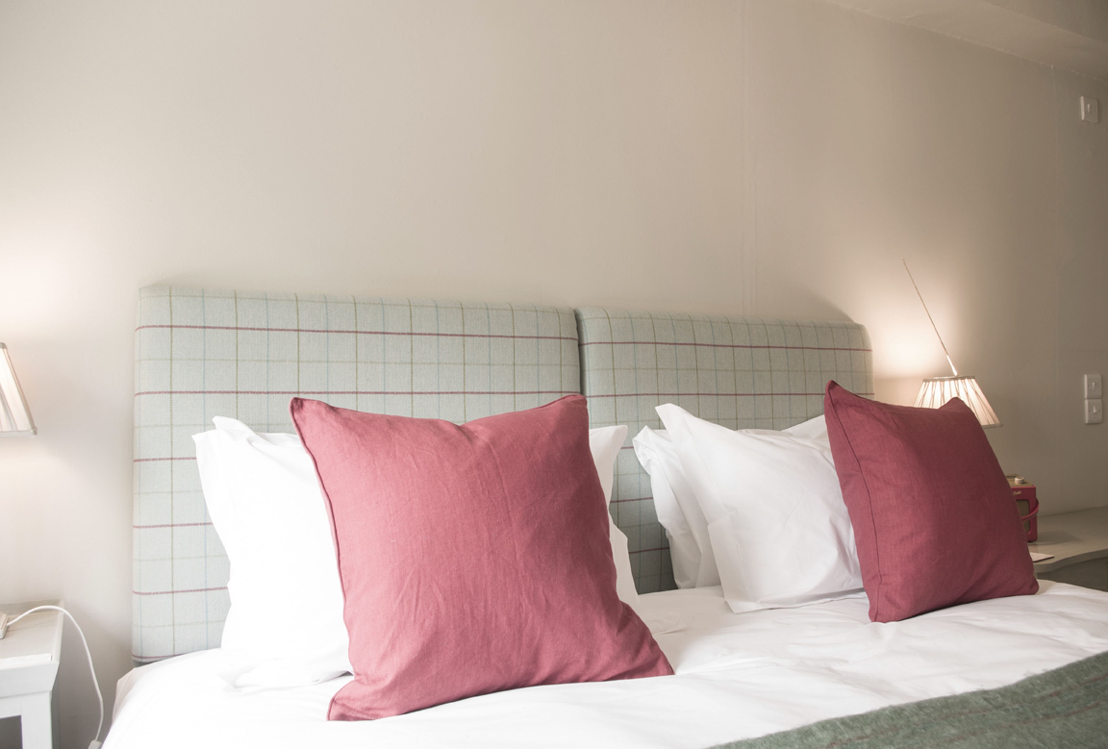 Una habitación de hotel con cama, almohadas, mesita de noche y lámpara.
