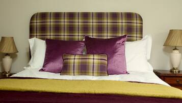 A neatly made bed with a plaid headboard, white and purple pillows, and a yellow throw blanket.