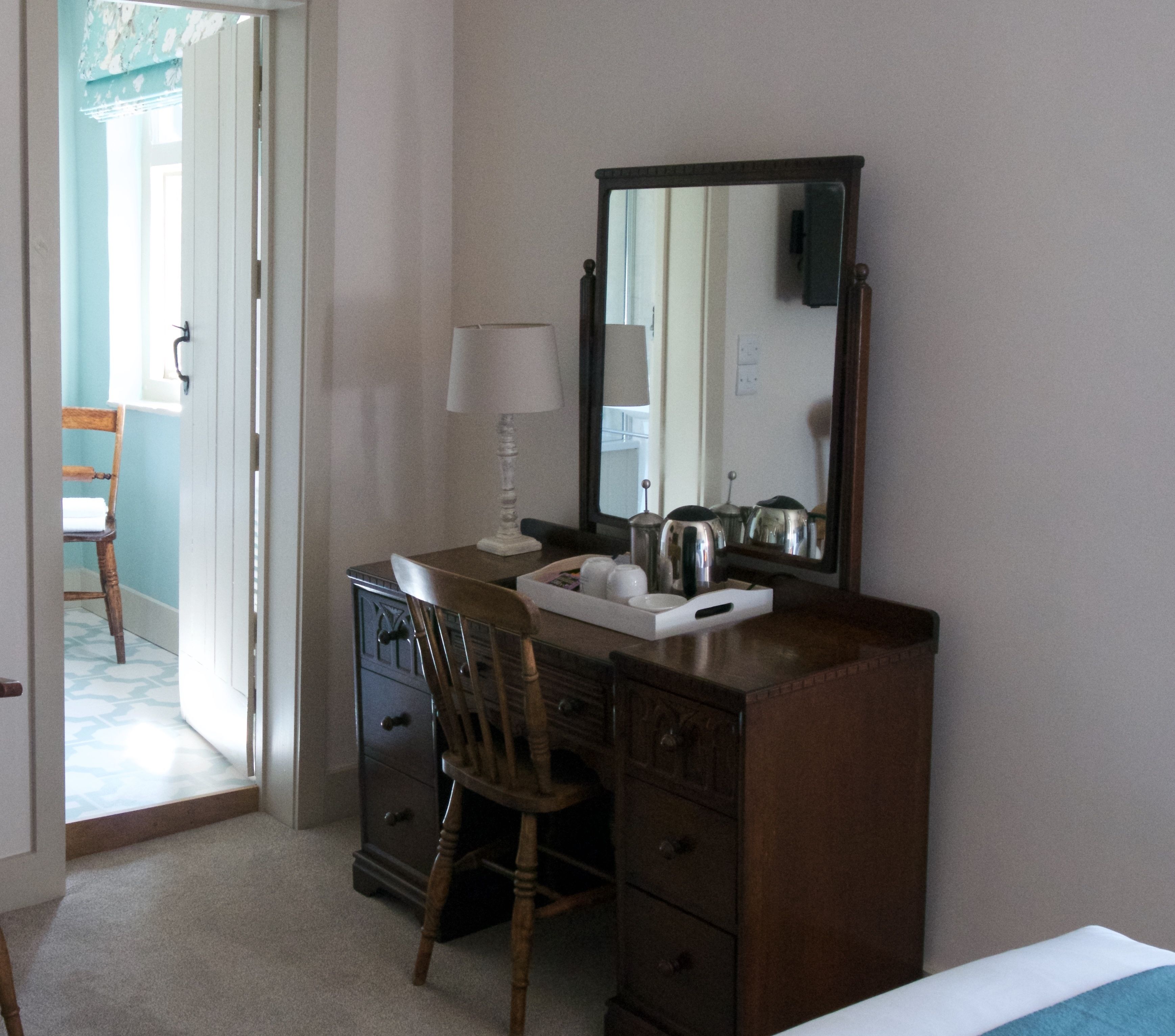 Habitación de hotel con tocador de madera, espejo, lámpara y una silla.
