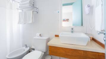 A modern bathroom with a white sink, vanity, bidet, toilet, and a towel rack with folded towels.