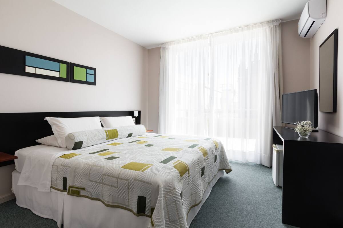 A hotel room with a bed, a desk, a TV, and a window with curtains.