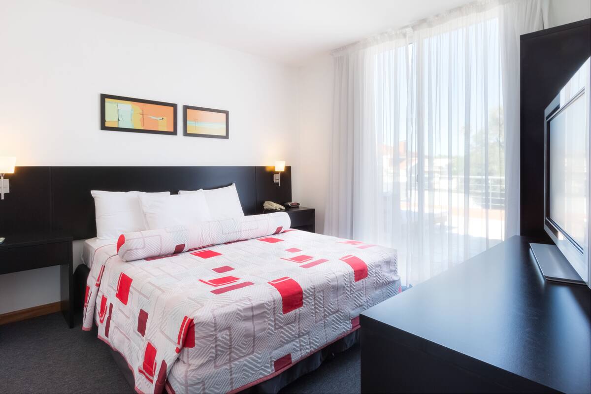 A hotel room with a bed, a TV, a nightstand, and a window with curtains.
