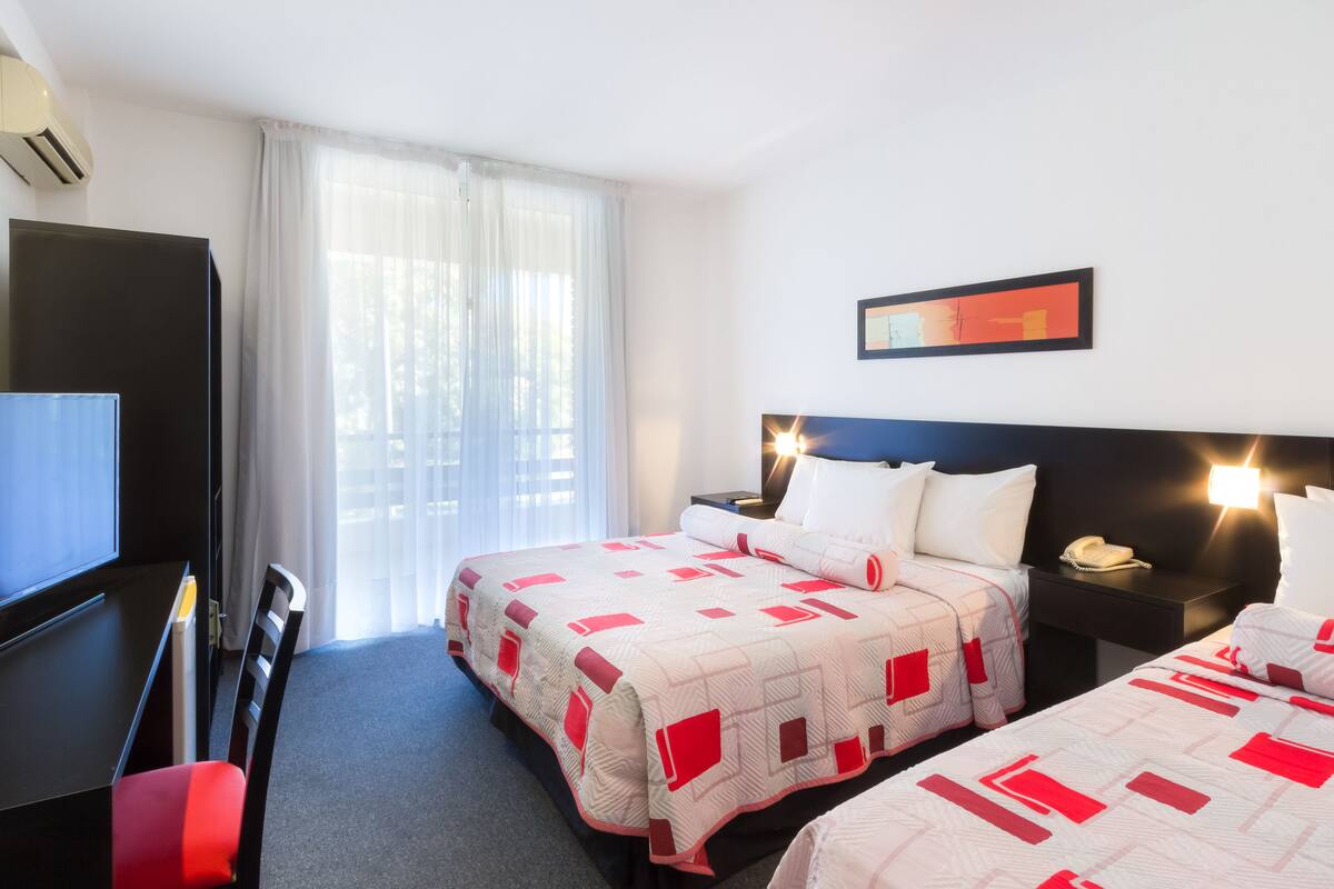 A hotel room with two beds, a desk, and a TV.