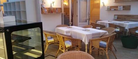 A dining area with wicker furniture and white tablecloths, a glass oven door, and a wooden wall with shelves.