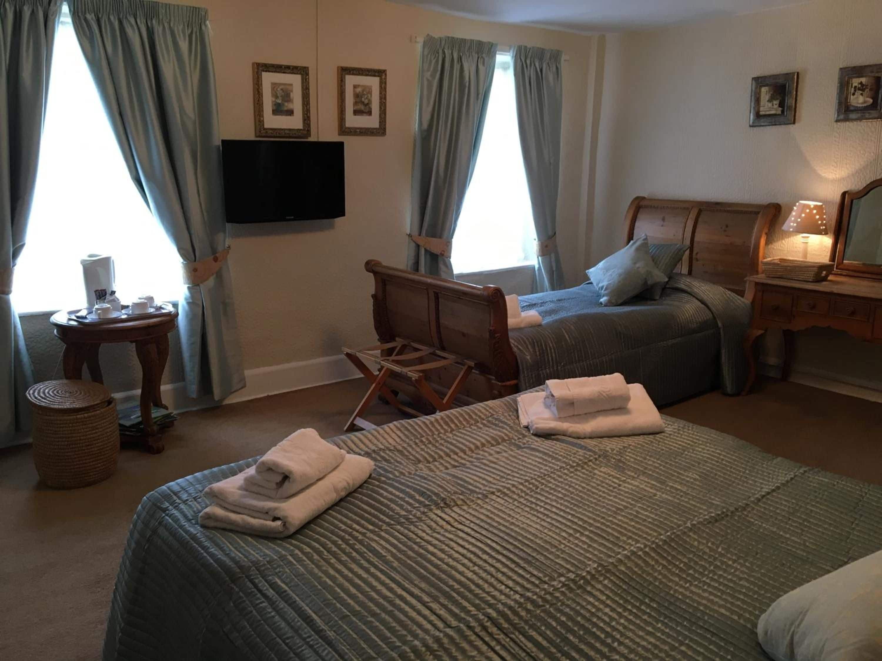 A hotel room with two beds, a television, a desk with a lamp, and a window with curtains.