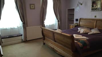 A bedroom with a wooden bed, a bench by the window, and a nightstand with a lamp.