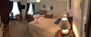 A hotel room with two beds, a desk, a chair, a lamp, and a television. - The Old Well Inn (Barnard Castle)