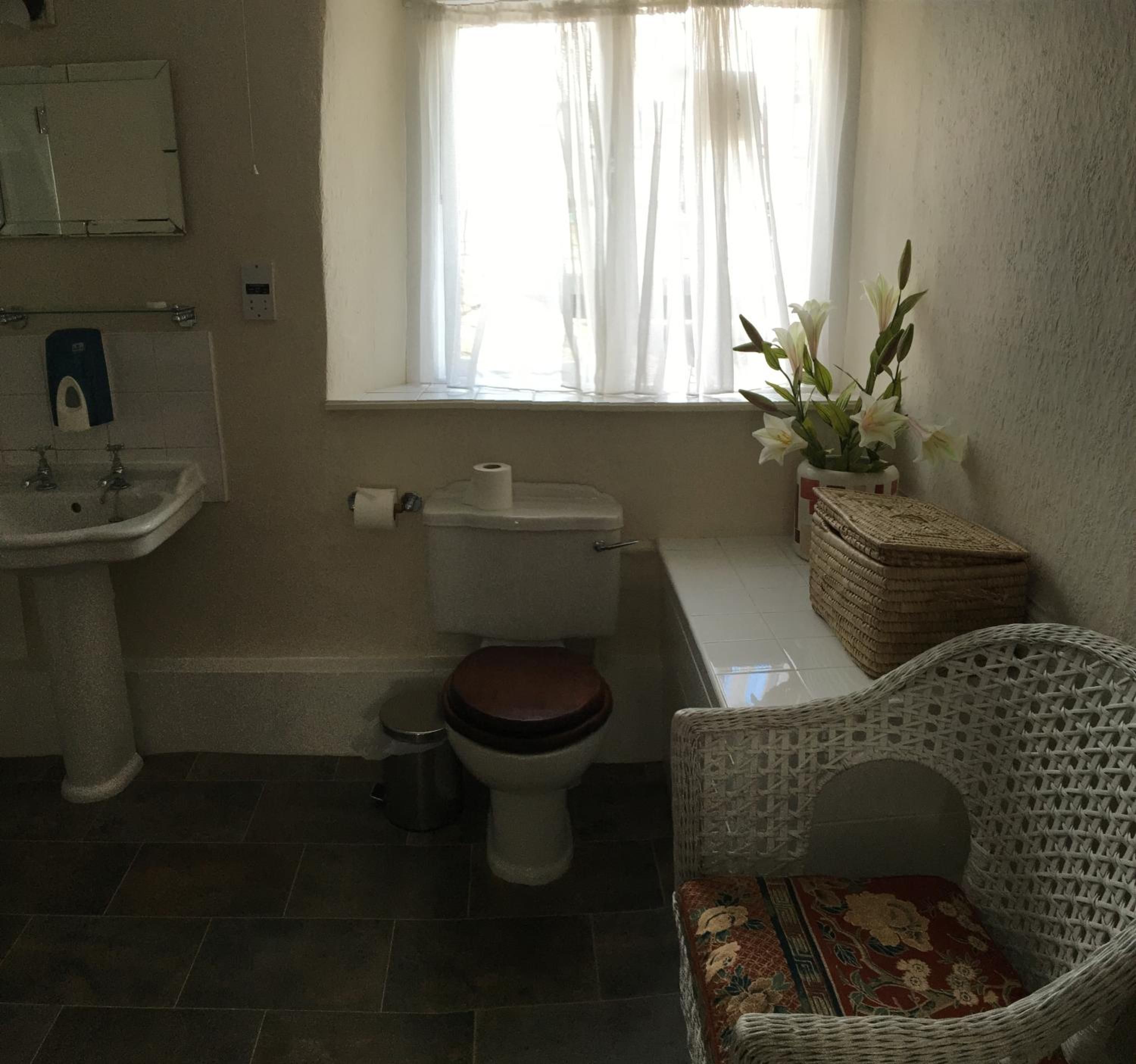 Une salle de bain avec des toilettes, un lavabo et une chaise en osier.