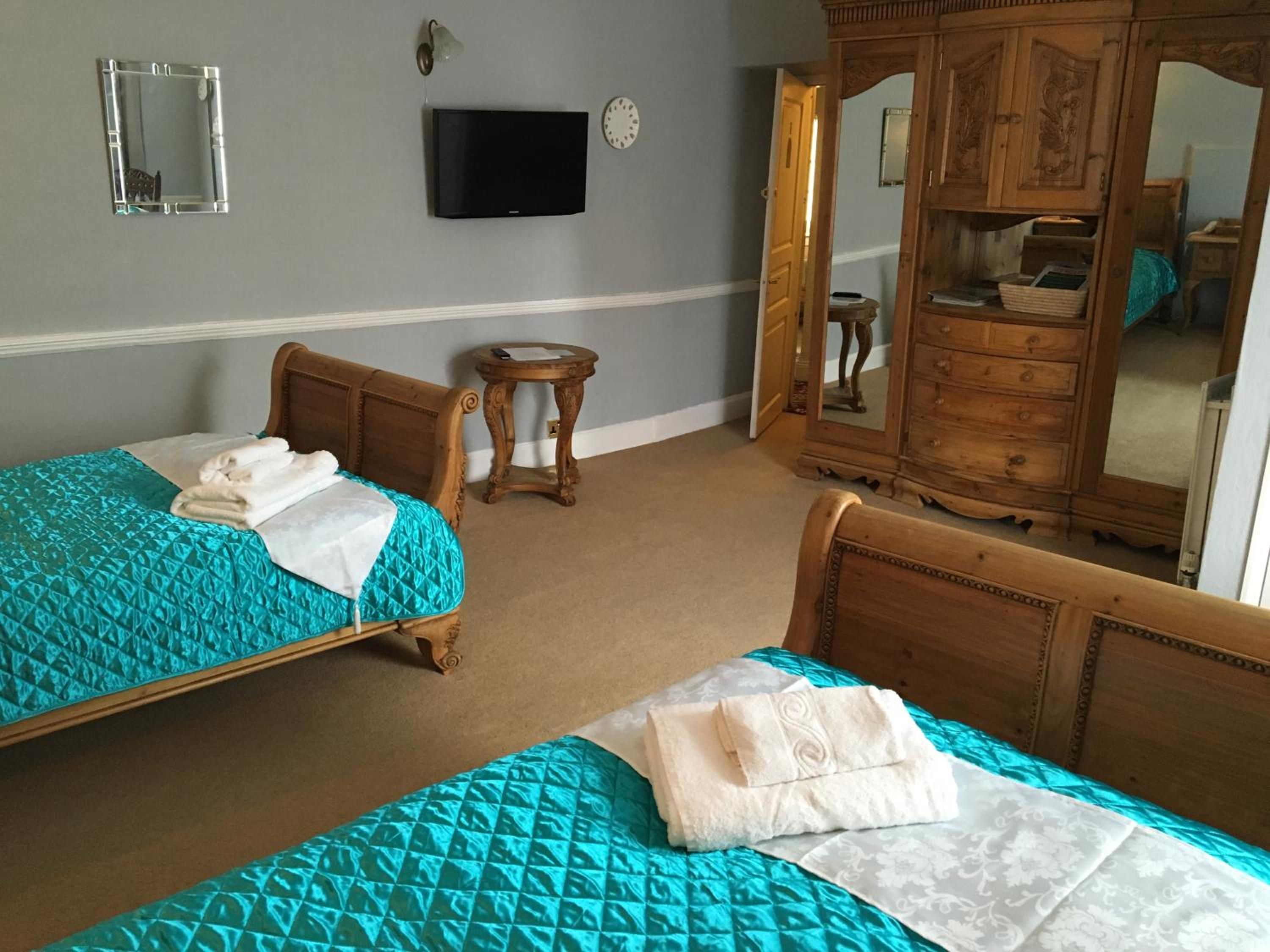 A hotel room with two beds, a television, a mirror, and a wooden wardrobe.