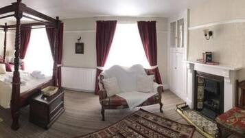 A four-poster bed with a canopy, a fireplace, a television mounted on the wall, and a small table with a chair.