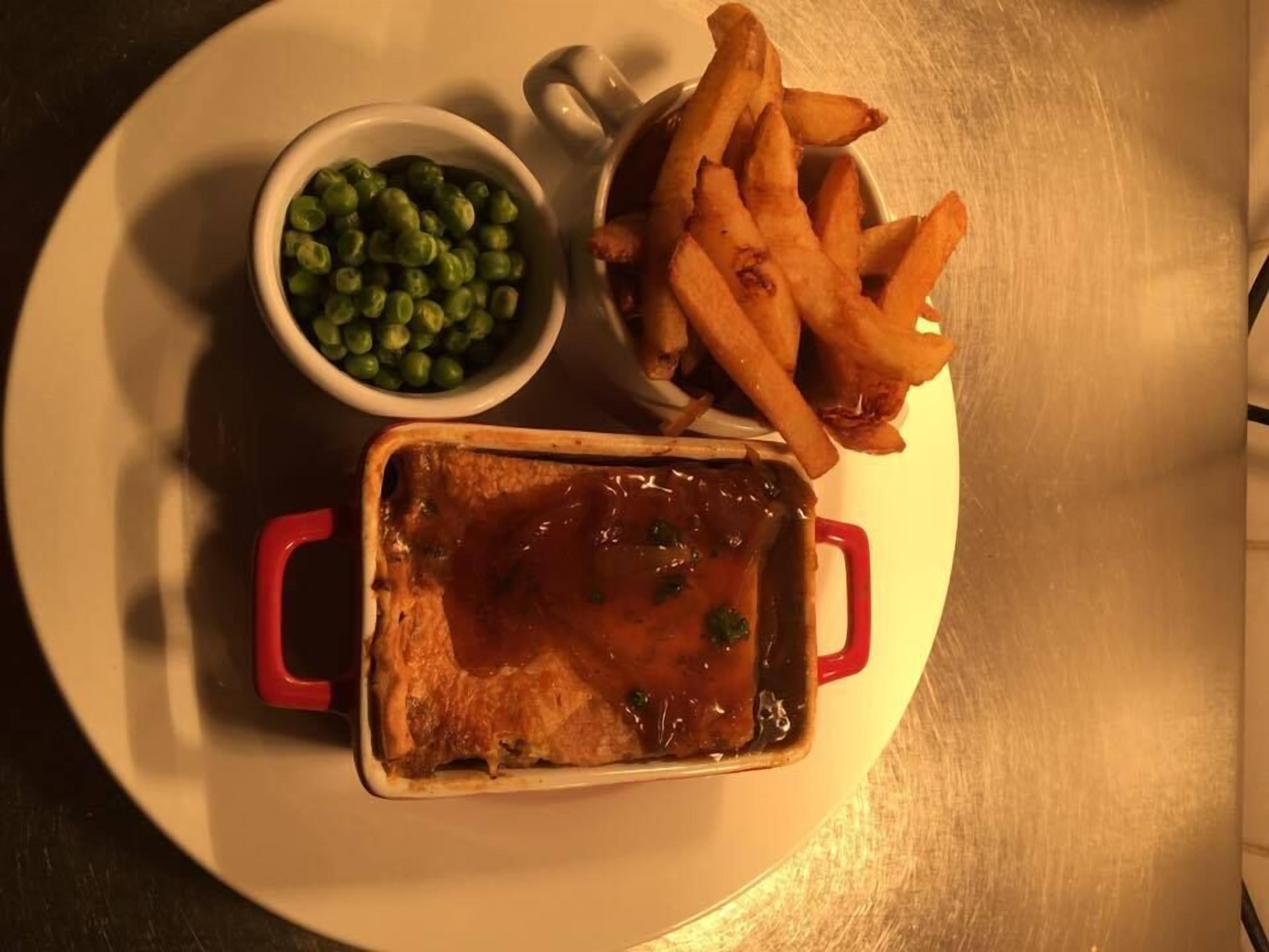 A meal consisting of a pie, French fries, and peas on a white plate.