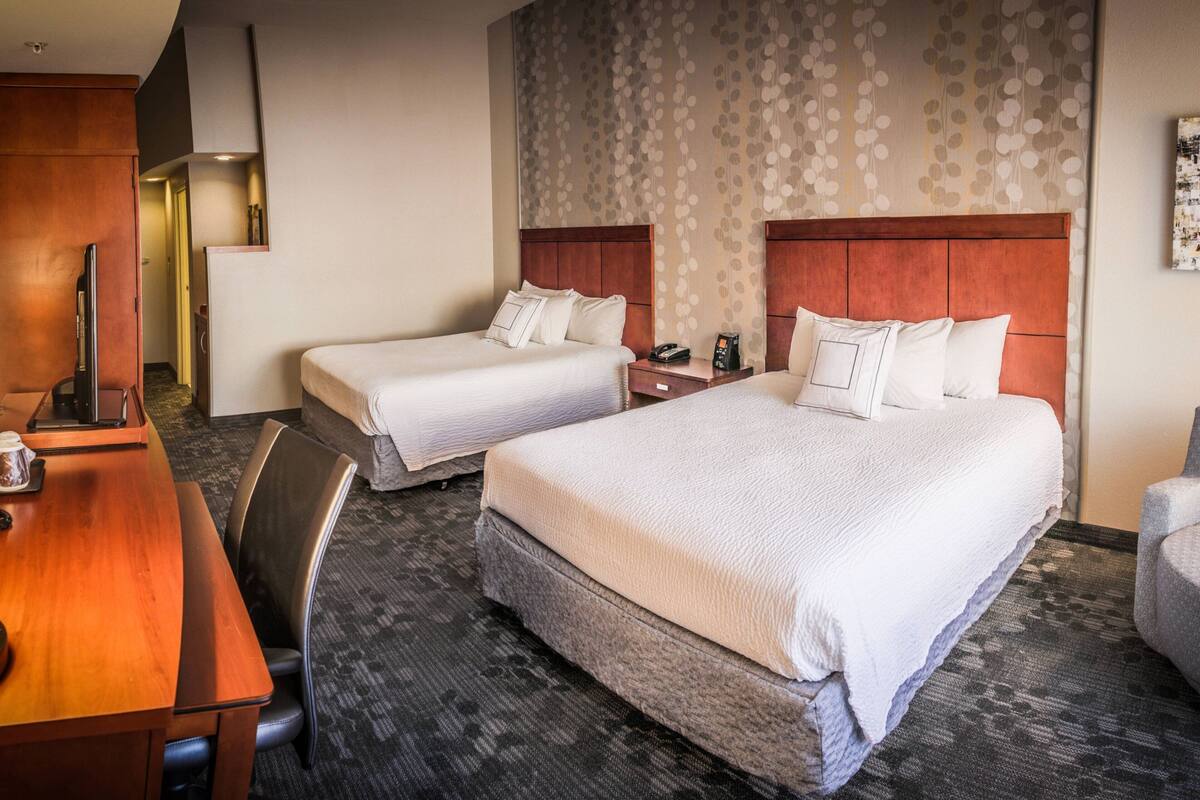 A hotel room with two beds, a desk, and a chair.