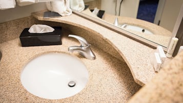 A bathroom sink with a granite countertop, a mirror, a towel dispenser, and a tissue box.